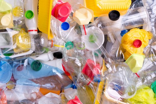 A large pile of assorted plastic waste, including empty bottles, caps, and containers of various shapes and sizes, predominantly made of transparent and colored plastics such as yellow, red, green, and blue. The waste is scattered across a flat surface, possibly an outdoor driveway or a designated rubbish collection area. The bottles feature different cap colours, with some caps removed and loose, and many bottles crumpled or flattened. The plastic items are piled loosely, with some overlapping and leaning against each other. The lighting appears natural, suggesting the photo was taken outdoors during daylight. This clutter exemplifies waste accumulation that a professional rubbish removal service like House Clearance Redhill would handle, often involving sorting, collection, and environmentally responsible disposal or recycling within the local area near Redhill.
